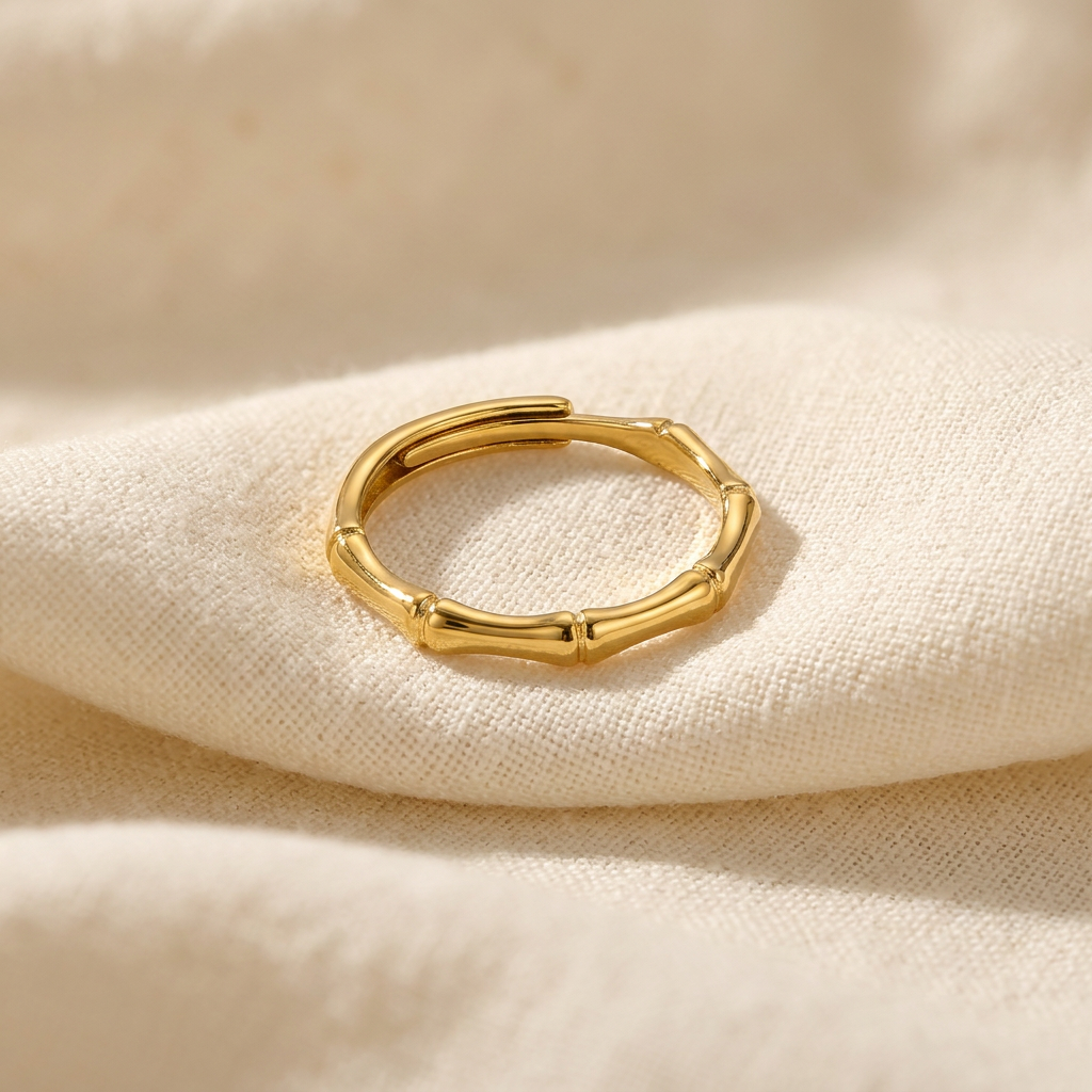 A gold bamboo ring with segmented stalk design and natural node details lying flat on a white background with soft natural shadows, showing the botanical texture, Asian-inspired natural form, and polished gold finish from above.
