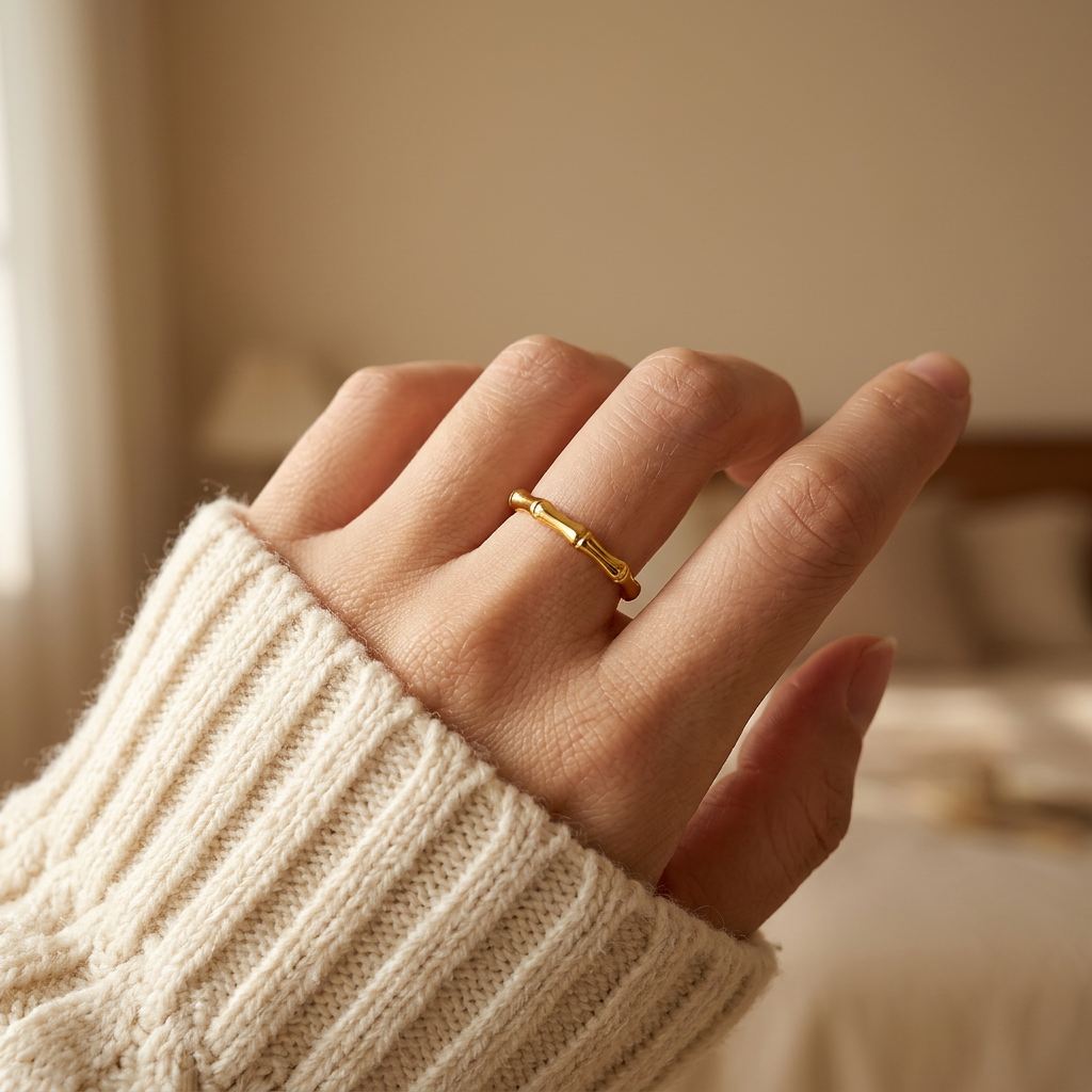 Close-up of a feminine hand wearing a gold bamboo ring with segmented stalk design, the botanical natural form resting on the finger. Soft natural lighting, warm beige linen background, natural skin texture with visible pores and slight imperfections.