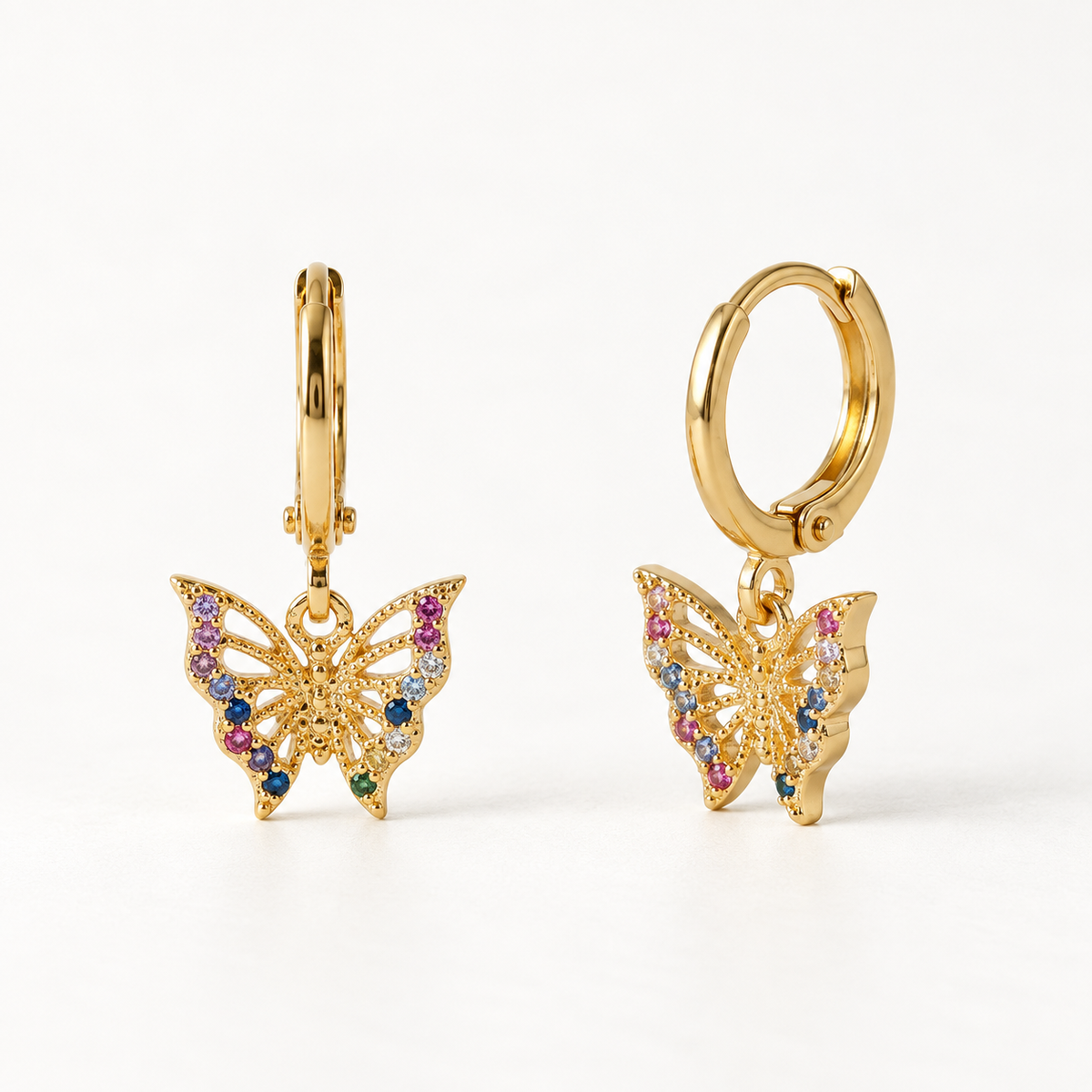 A pair of 18k gold huggie hoop earrings with dangling butterfly charms covered in multicolored pave crystals, shown from front and side angles on a clean white background displaying the vibrant rainbow stone detail and hinged closure.
