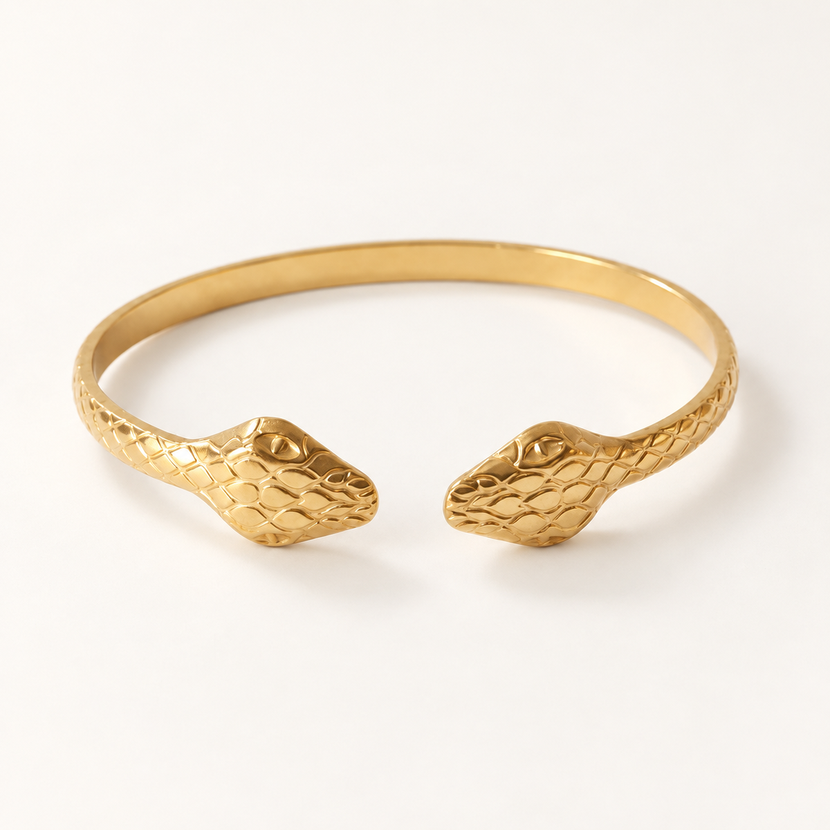 A gold double-headed snake bangle cuff with textured scale pattern and detailed serpent heads on both ends, shown from front and side angles on a clean white background displaying the open cuff design and intricate scale texture.