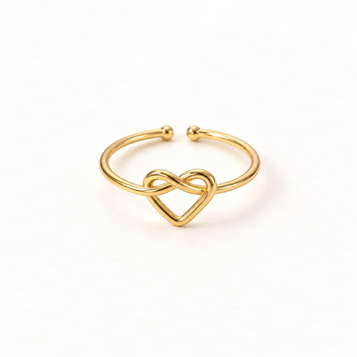 A gold infinity heart ring with continuous loop forming an intertwined heart shape, open adjustable band with textured rope detail, shown from front and side angles on a clean white background displaying the eternal love symbolism, delicate interwoven design, and polished gold finish.