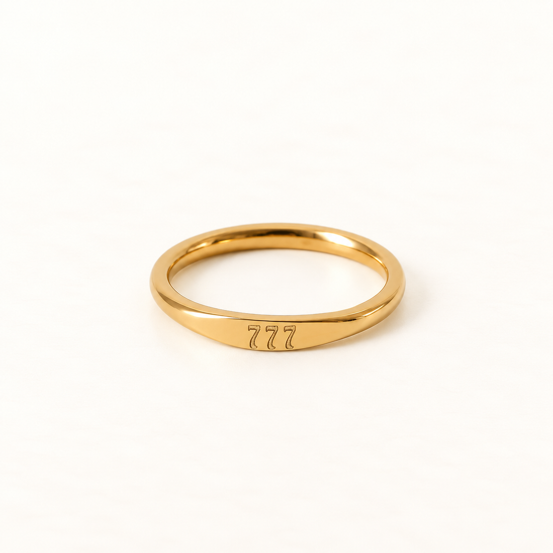 A gold angel number ring with "777" engraved on the band, slim minimalist design with etched numerals, shown from front and side angles on a clean white background displaying the spiritual luck symbol, delicate band, and polished gold finish.