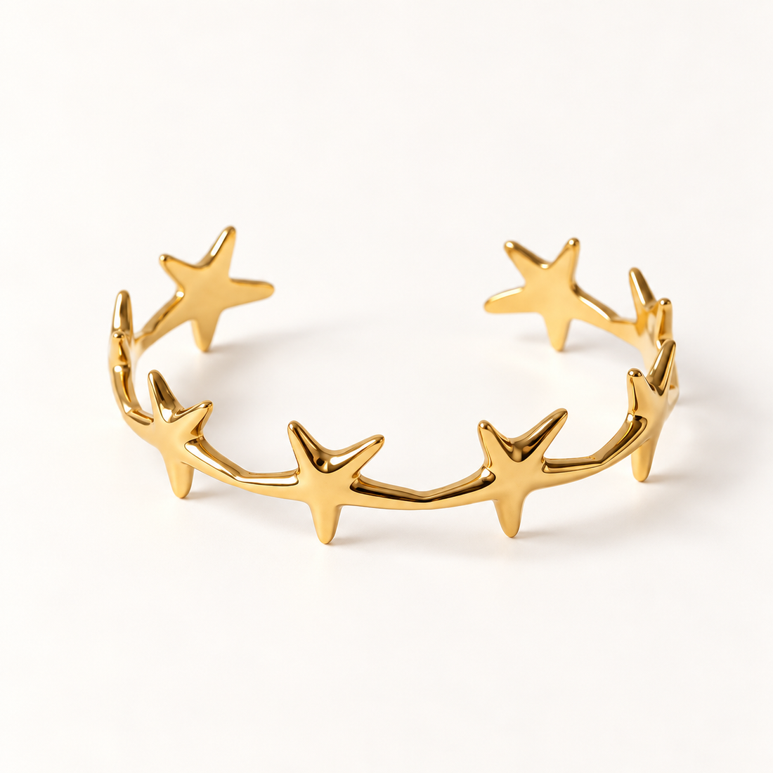 A gold star cuff bracelet with multiple five-point stars forming an open celestial band, shown from front and side angles on a clean white background displaying the polished star shapes, open cuff design, and cosmic constellation aesthetic.