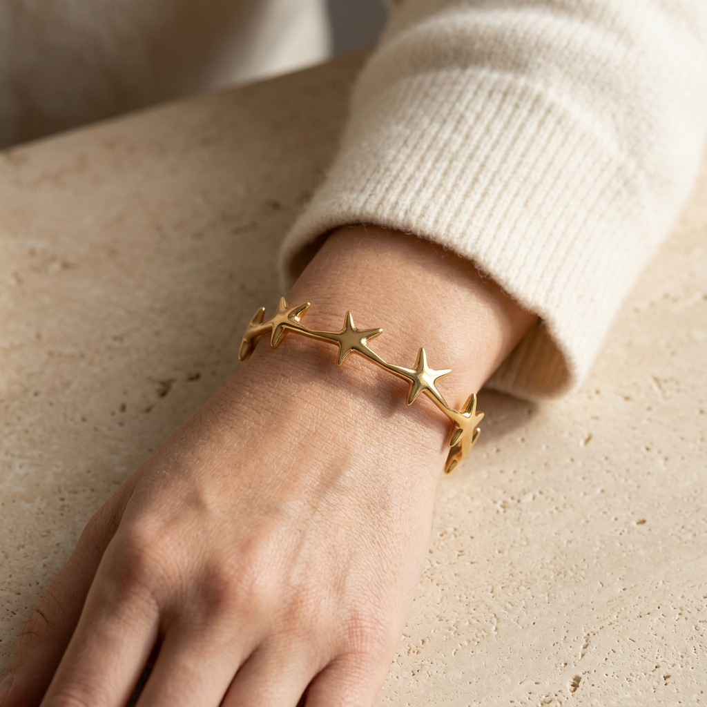 Close-up of a feminine wrist wearing a gold star cuff bracelet with multiple five-point stars forming a celestial band, the constellation design wrapping around the wrist bone. Soft natural lighting, warm beige linen background, natural skin texture with visible pores and slight imperfections.