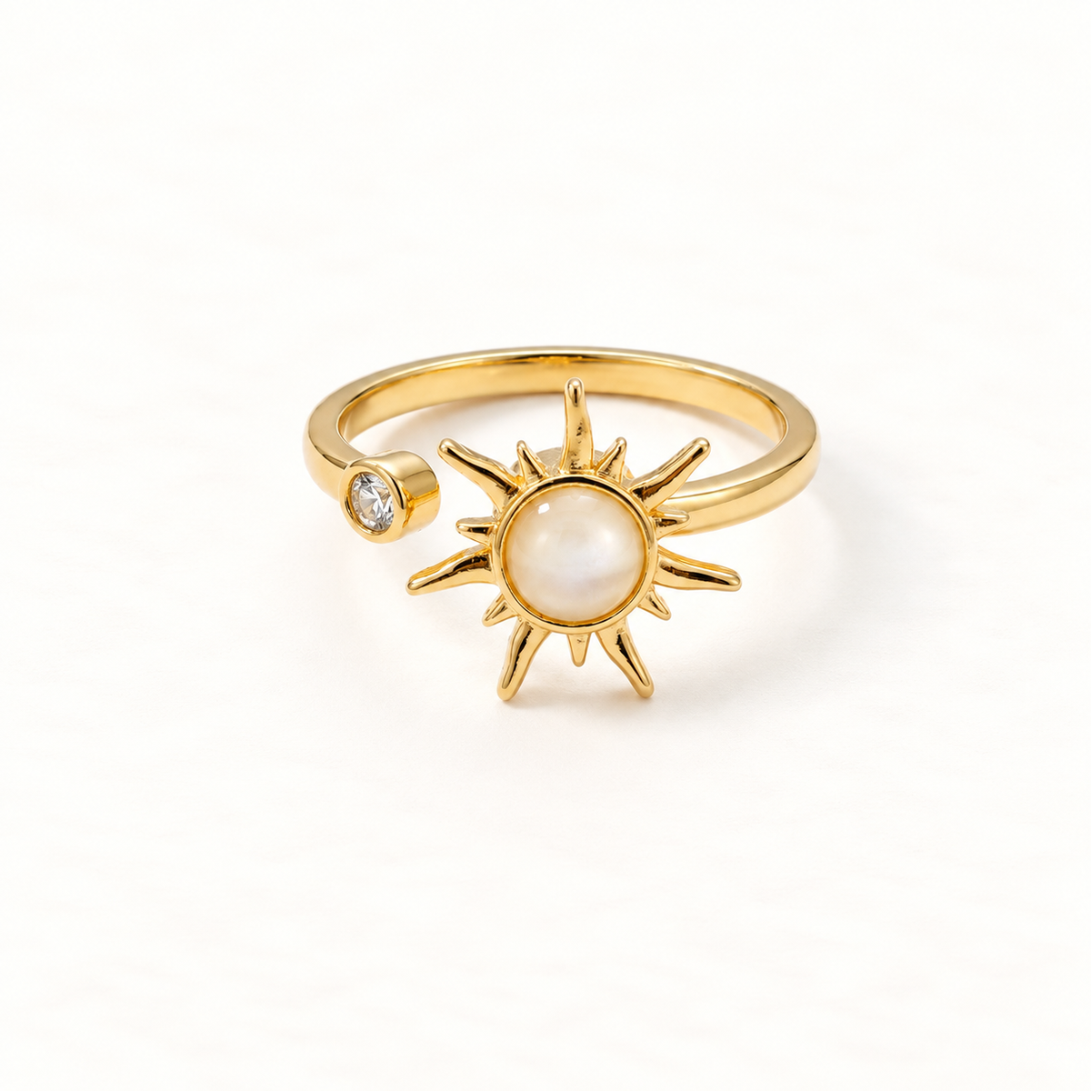 A gold sun spinner ring with rotating sunburst center, pearlescent moonstone center and small clear crystal accent, open adjustable band, shown from front and side angles on a clean white background displaying the kinetic celestial design, radiating rays, and polished gold finish.