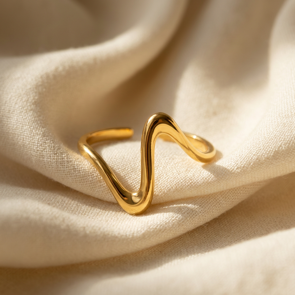 A gold wave heartbeat ring with zigzag pulse line design and smooth curved peaks lying flat on a white background with soft natural shadows, showing the rhythmic line pattern, sculptural wave form, and polished gold finish from above.