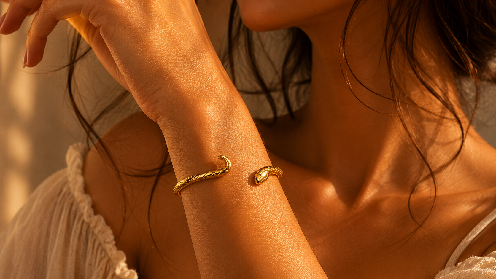 Close-up editorial image of gold snake bangle bracelet on model wrist with warm cinematic lighting and soft feminine aesthetic.