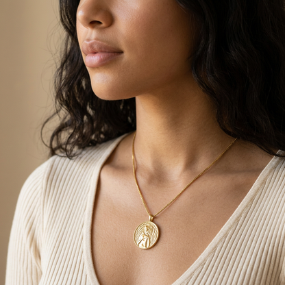 Close-up of a feminine neck and collarbone wearing a gold Aphrodite love coin necklace, the detailed medallion with goddess of beauty and dove resting at the chest. Soft natural lighting, warm beige linen background, natural skin texture with visible pores and slight imperfections.