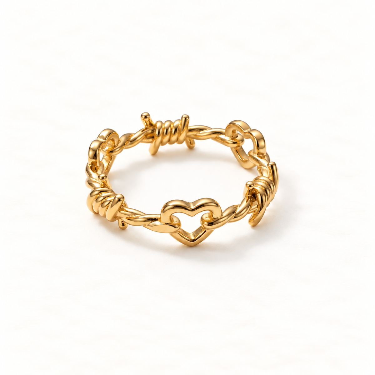 A gold barbed wire heart ring with twisted wire texture and open heart center, edgy punk-inspired design with wrapped wire details, open adjustable band, shown from front and side angles on a clean white background displaying the rebellious romantic symbolism, intricate wirework, and polished gold finish.