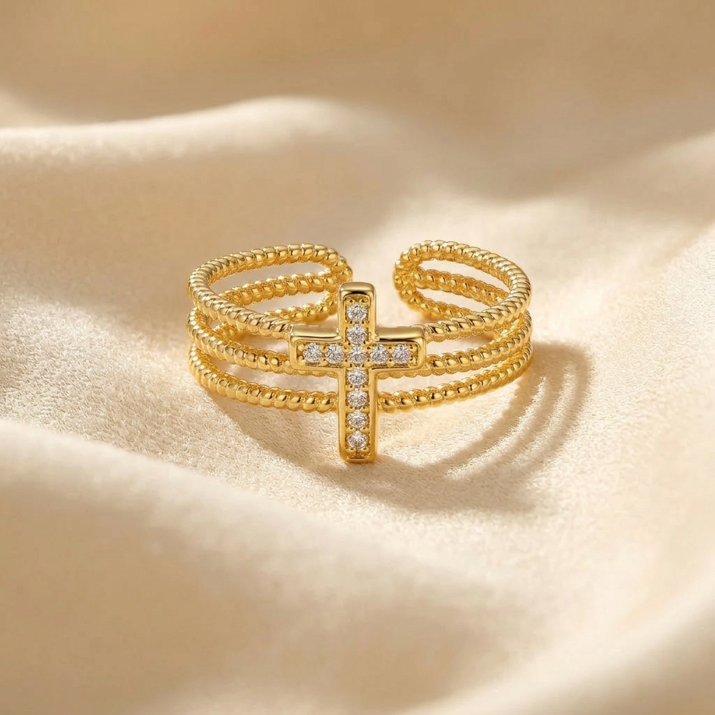 A gold beaded cross pave ring with three rows of ball chain bands and crystal-encrusted cross centerpiece lying flat on a white background with soft natural shadows, showing the sparkling stone detail, textured beaded texture, and polished gold finish from above.