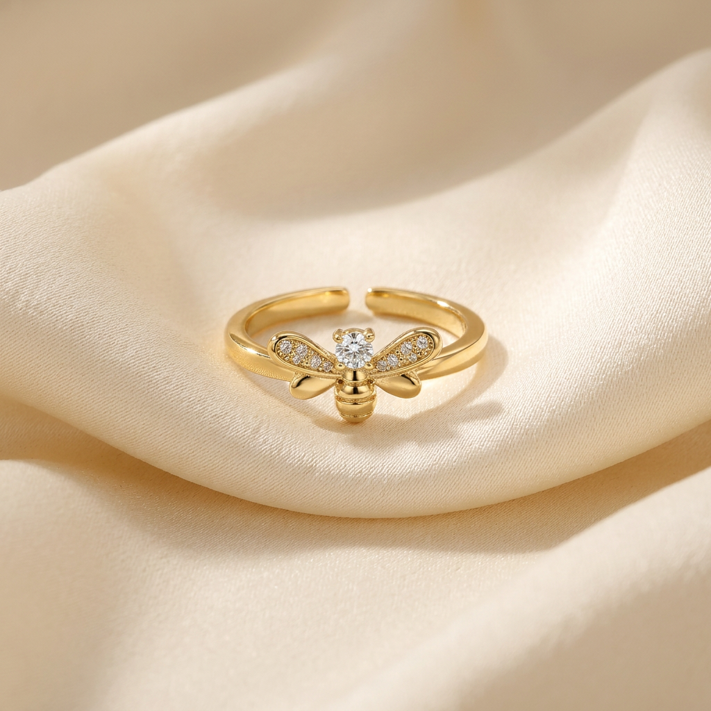 A gold bee ring with detailed insect body, pave crystal wings and body segments lying flat on a white background with soft natural shadows, showing the intricate nature-inspired design, sparkling stone detail, and polished gold finish from above.
