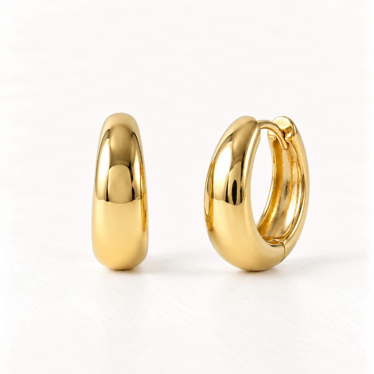 A pair of 18k gold bold dome huggie hoop earrings with thick polished rounded profile, shown from front and side angles on a clean white background displaying the substantial smooth reflective surface and hinged closure.