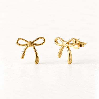 A pair of 18k gold bow stud earrings on a clean white background, one facing forward showing the delicate ribbon bow detail, the other angled to display the post and butterfly backing.