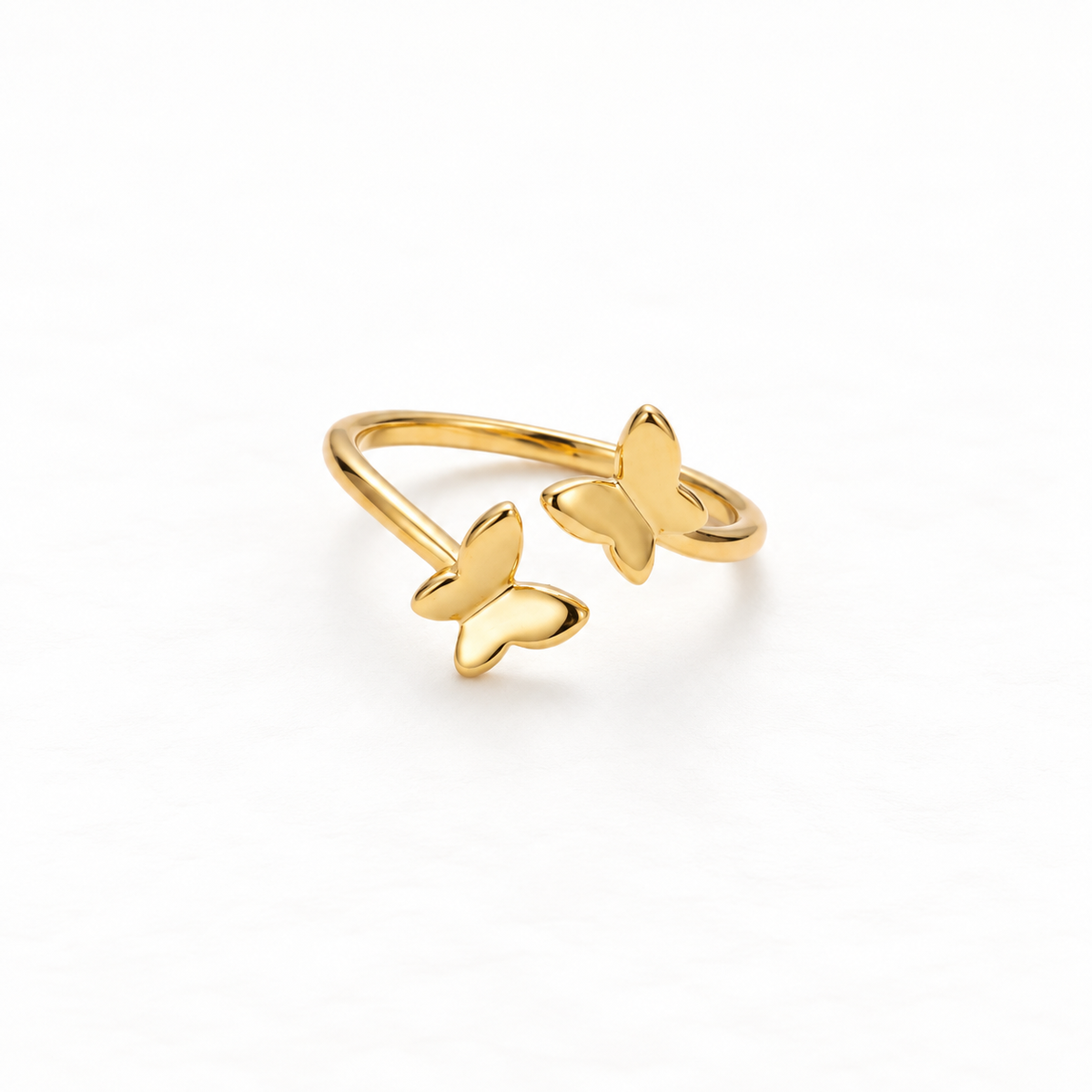 A gold butterfly ring with two delicate butterfly silhouettes on open adjustable band, nature-inspired design with detailed wing texture, shown from front and side angles on a clean white background displaying the fluttering pair, intricate wing veins, and polished gold finish.