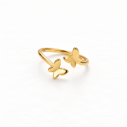 A gold butterfly ring with two delicate butterfly silhouettes on open adjustable band, nature-inspired design with detailed wing texture, shown from front and side angles on a clean white background displaying the fluttering pair, intricate wing veins, and polished gold finish.