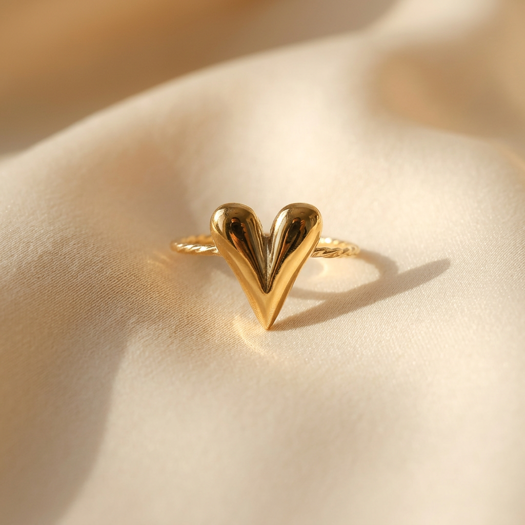 A gold chevron heart ring with V-shaped arrow design forming a heart silhouette and twisted rope texture band lying flat on a white background with soft natural shadows, showing the geometric love symbol, intricate rope detail, and polished gold finish from above.
