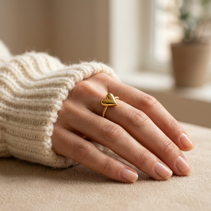Close-up of a feminine hand wearing a gold chevron heart ring with V-shaped arrow design and twisted rope texture band, the geometric love symbol resting on the finger. Soft natural lighting, warm beige linen background, natural skin texture with visible pores and slight imperfections.