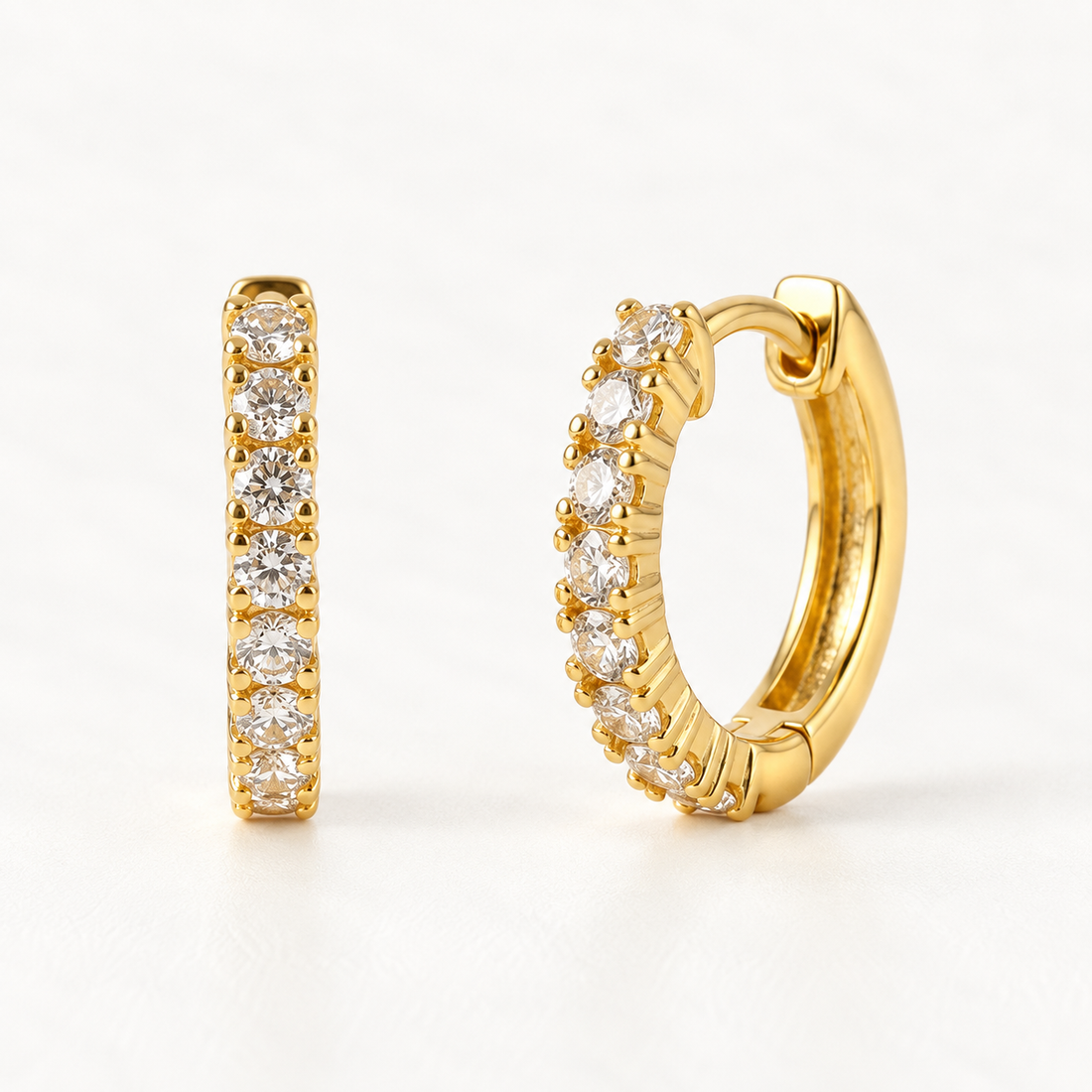 A pair of 18k gold classic pave huggie hoop earrings with clear crystals set along the front half, shown from front and side angles on a clean white background displaying the sparkling stone detail and hinged closure.