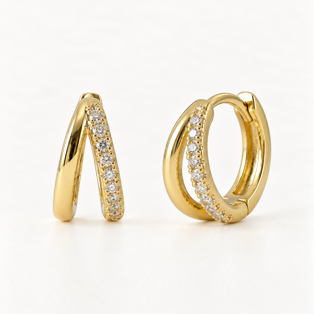A pair of 18k gold crisscross huggie hoop earrings with double intersecting bands and clear pave crystals, shown from front and side angles on a clean white background displaying the sparkling X-shaped detail and hinged closure.
