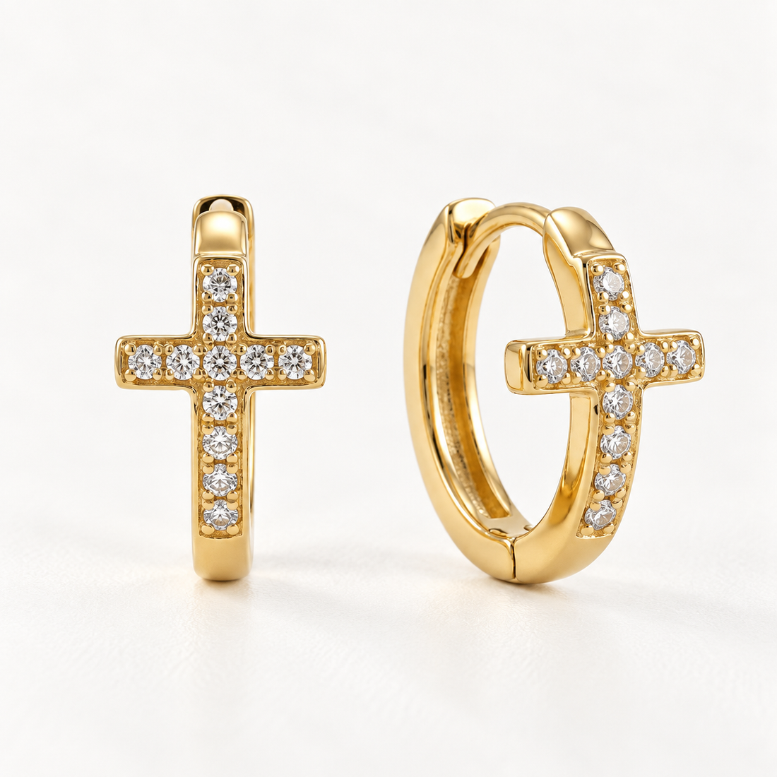 A pair of 18k gold cross-shaped huggie hoop earrings with clear pave crystals along the edges, shown from front and side angles on a clean white background displaying the hinged closure and sparkling stone detail.