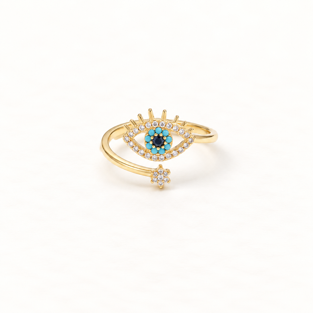 A gold crown evil eye ring with regal tiara detail above, turquoise blue center stone surrounded by clear crystals, and floral star accent below, open adjustable band, shown from front and side angles on a clean white background displaying the protective royal symbolism, intricate stone setting, and polished gold finish.
