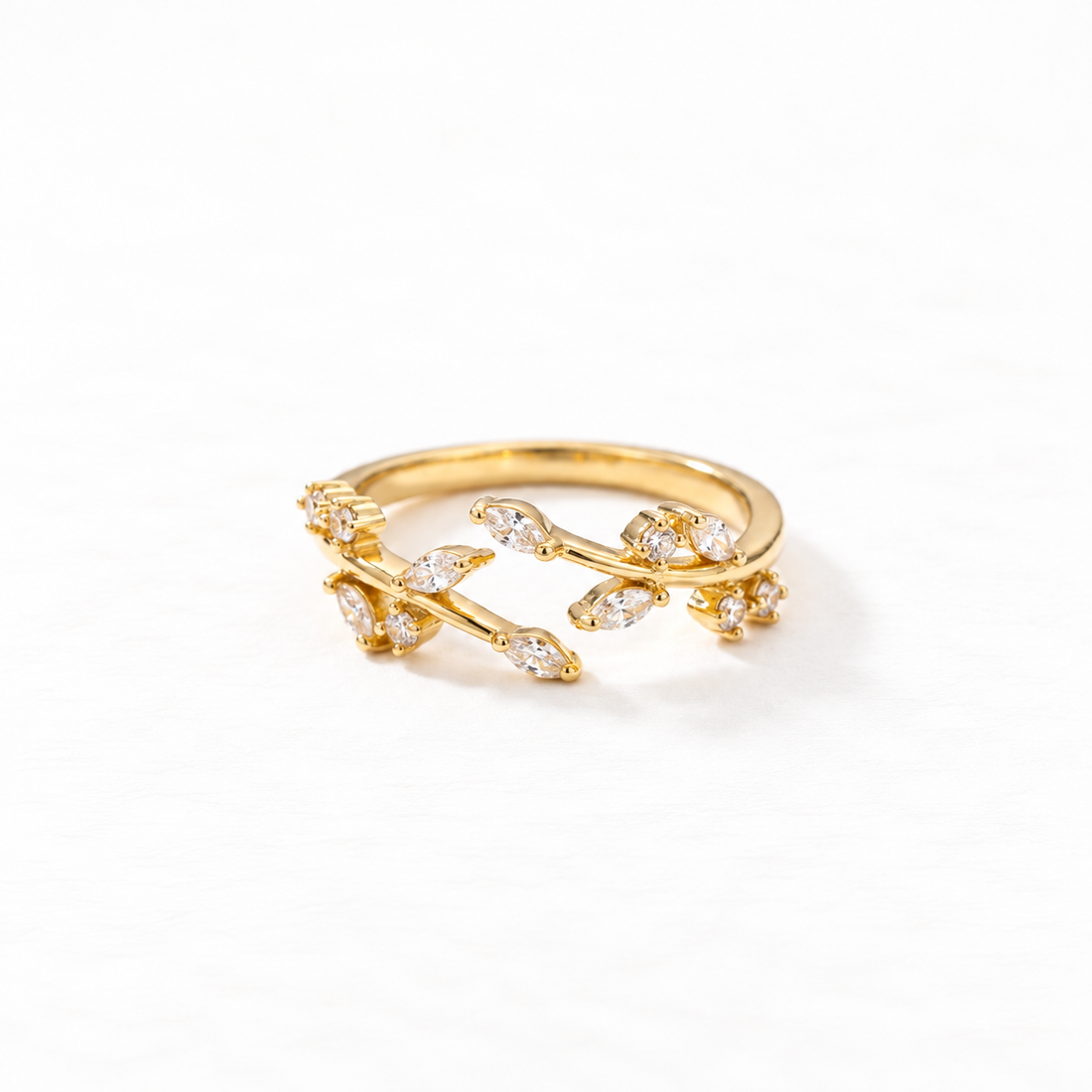 A gold crystal vine ring with winding branch design and clear pave stones set in leaf-shaped settings, delicate botanical open band, shown from front and side angles on a clean white background displaying the nature-inspired sparkle, intricate twig texture, and polished gold finish.