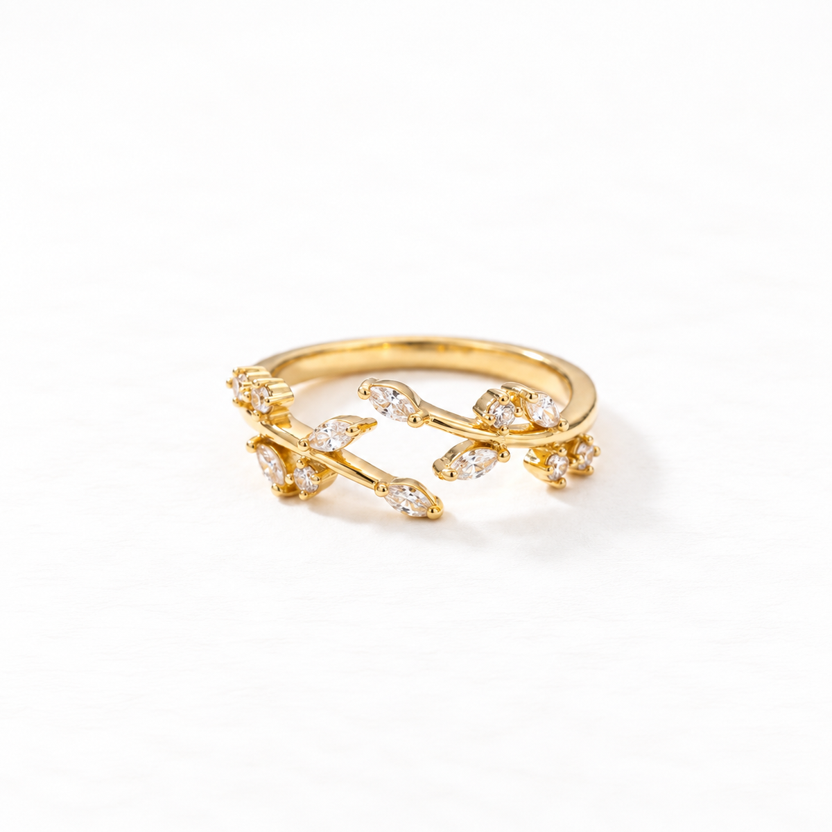A gold crystal vine ring with winding branch design and clear pave stones set in leaf-shaped settings, delicate botanical open band, shown from front and side angles on a clean white background displaying the nature-inspired sparkle, intricate twig texture, and polished gold finish.