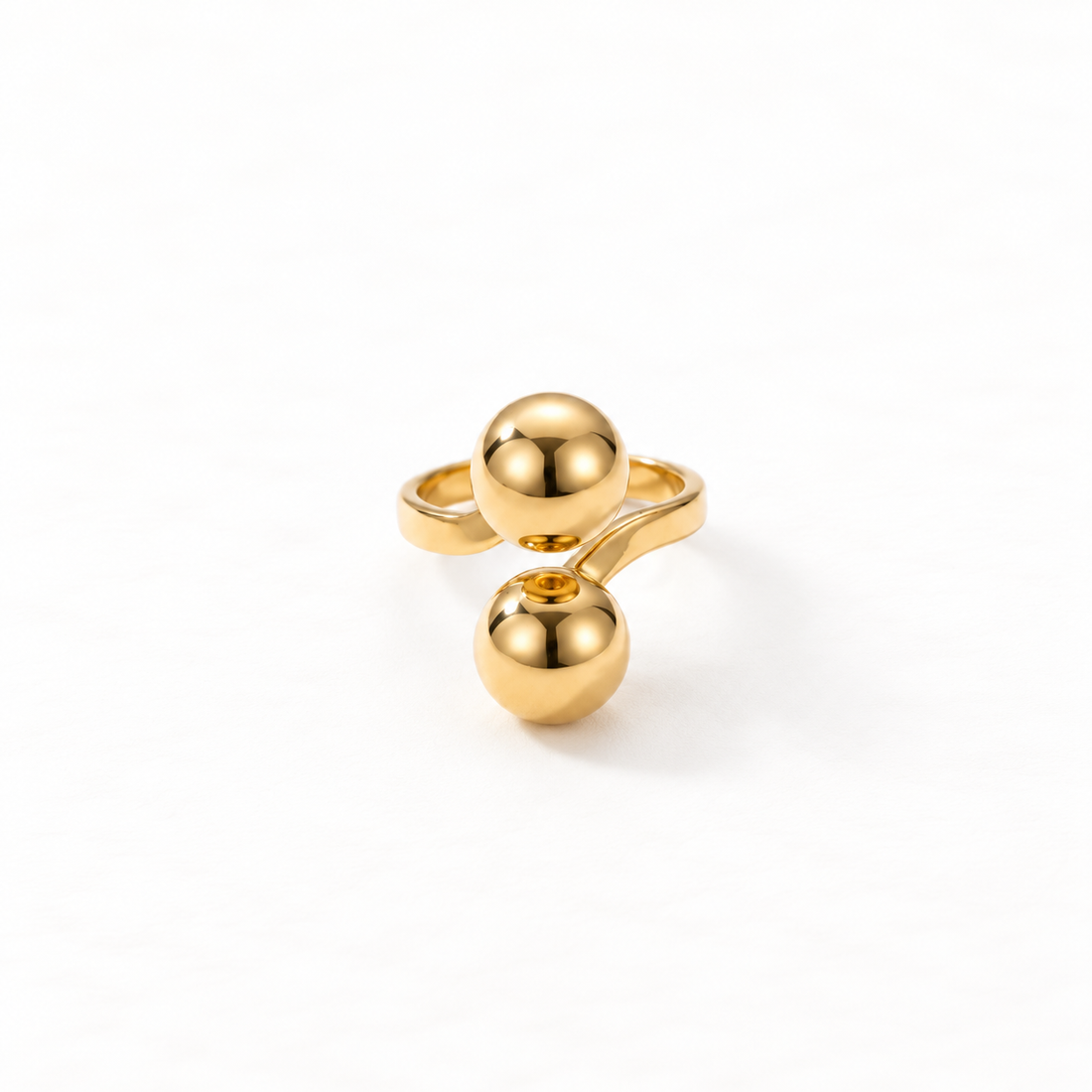 A gold double ball ring with two large polished spherical orbs on open adjustable band, modern minimalist statement design, shown from front and side angles on a clean white background displaying the sculptural spheres, sleek reflective surface, and polished gold finish.
