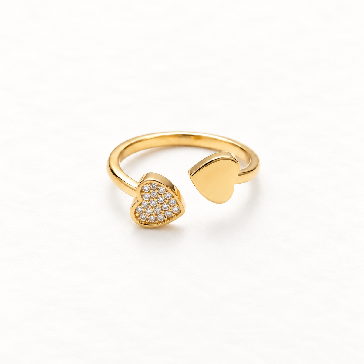 A gold double heart ring with one pave crystal-encrusted heart and one plain polished heart on open adjustable band, asymmetrical romantic design, shown from front and side angles on a clean white background displaying the sparkling contrast, dual heart symbolism, and polished gold finish.