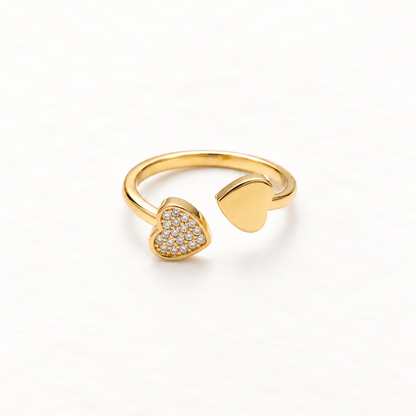 A gold double heart ring with one pave crystal-encrusted heart and one plain polished heart on open adjustable band, asymmetrical romantic design, shown from front and side angles on a clean white background displaying the sparkling contrast, dual heart symbolism, and polished gold finish.