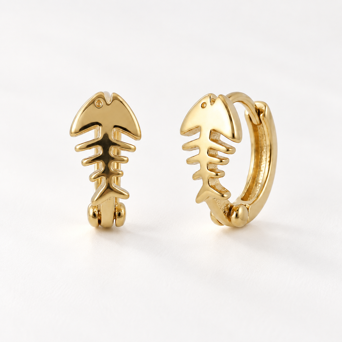 A pair of 18k gold fishbone-shaped huggie hoop earrings with skeletal rib detail, shown from front and side angles on a clean white background displaying the hinged closure and sculptural bone structure.