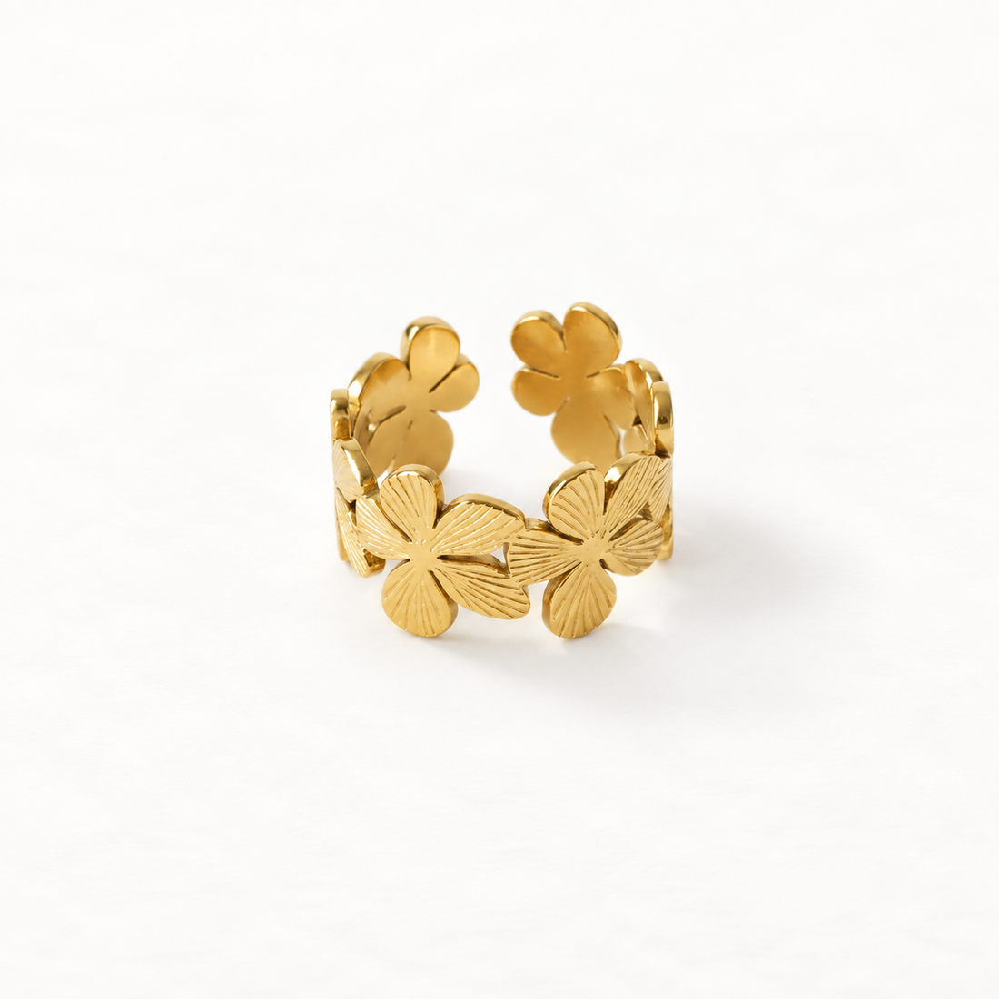 A gold flower band ring with multiple four-petal blossoms encircling the open adjustable band, textured petal detail on each bloom, shown from front and side angles on a clean white background displaying the continuous floral garden design, intricate botanical texture, and polished gold finish.