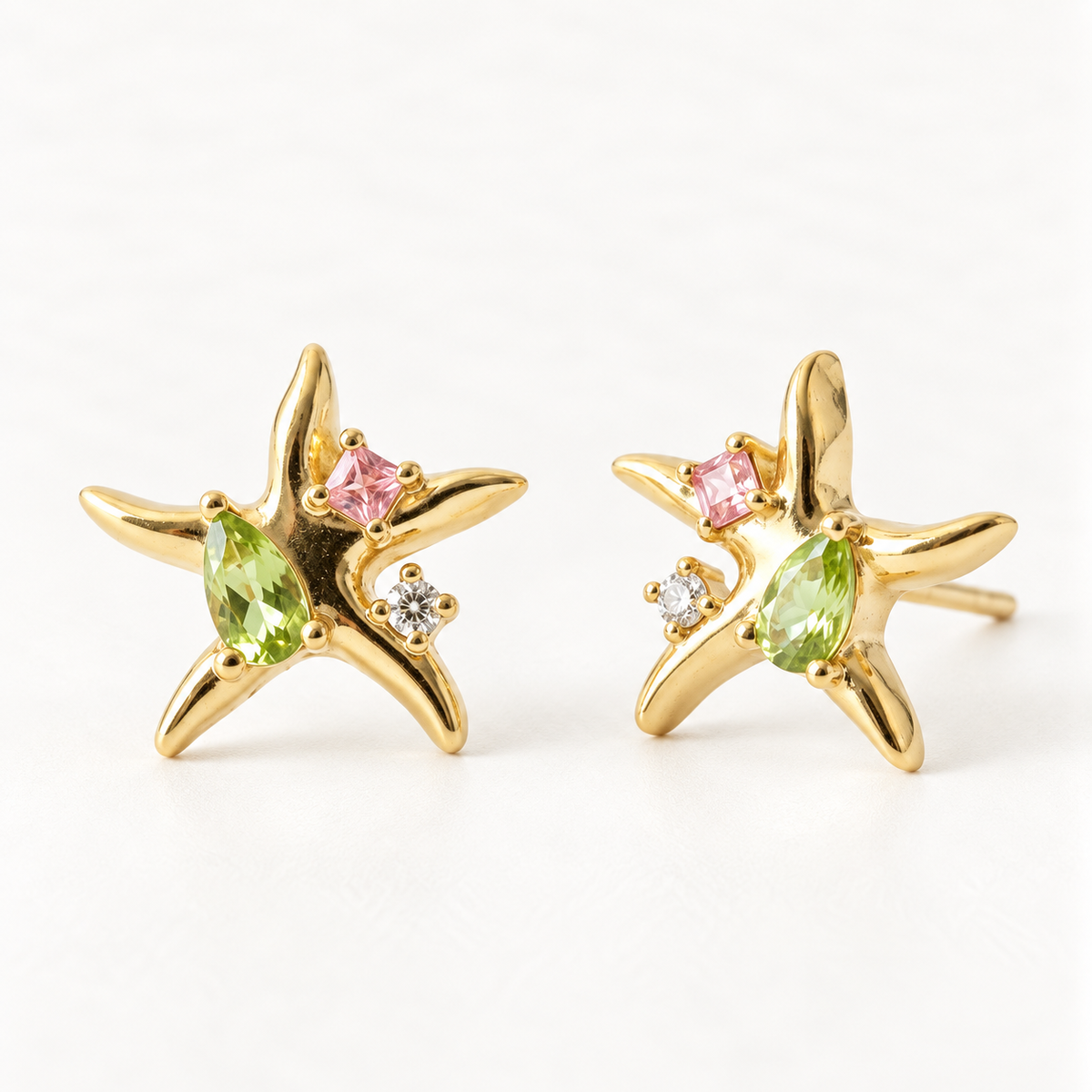 A pair of 18k gold starfish-shaped stud earrings with green peridot and pink tourmaline gemstones, shown from front and side angles on a clean white background displaying the colorful sea-inspired stone detail and post with butterfly backing.