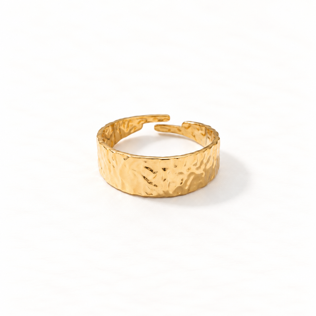 A gold hammered band ring with wide textured surface and organic dimpled pattern, open adjustable band with tapered ends, shown from front and side angles on a clean white background displaying the artisan hammered texture, substantial presence, and polished gold finish.