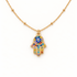 A gold Hamsa hand pave necklace with colorful crystal-encrusted palm, blue evil eye center, and rainbow stones on fingers, protective amulet design on delicate chain, shown from front and side angles on a clean white background displaying the vibrant multicolor sparkle, intricate hand detail, and polished gold finish.