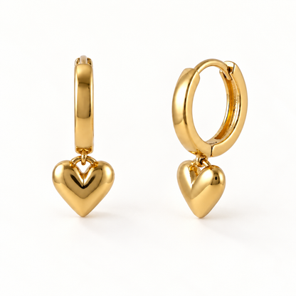A pair of 18k gold huggie hoop earrings with dangling polished heart charms, shown from front and side angles on a clean white background displaying the hinged closure and puffed heart detail.