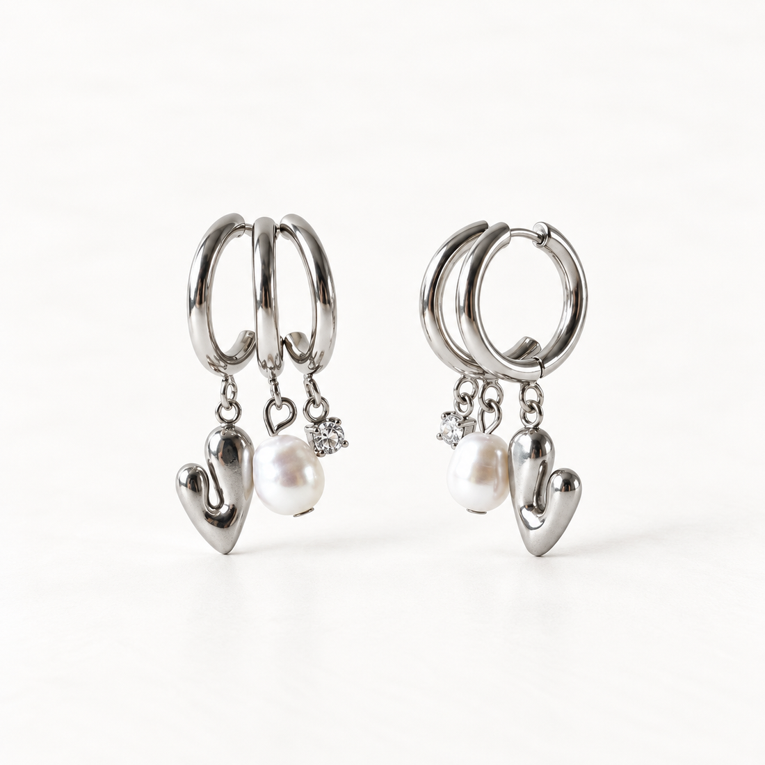 A pair of sterling silver huggie hoop earrings with dangling polished heart charms and white freshwater pearl accents, shown from front and side angles on a clean white background displaying the romantic charm detail and hinged closure.