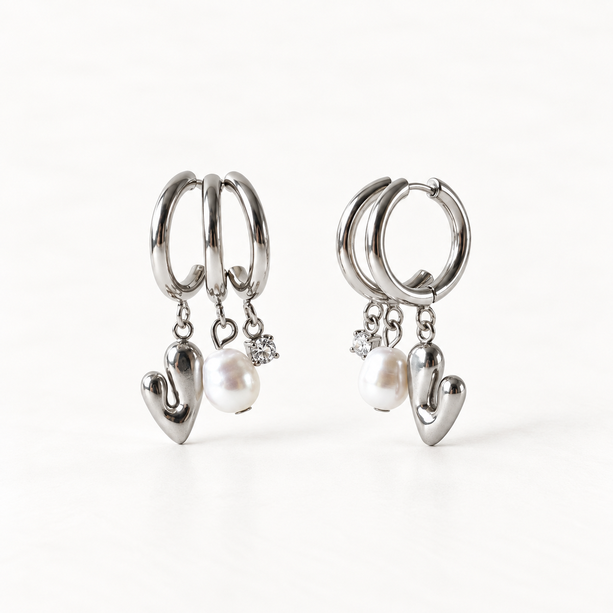 A pair of sterling silver huggie hoop earrings with dangling polished heart charms and white freshwater pearl accents, shown from front and side angles on a clean white background displaying the romantic charm detail and hinged closure.