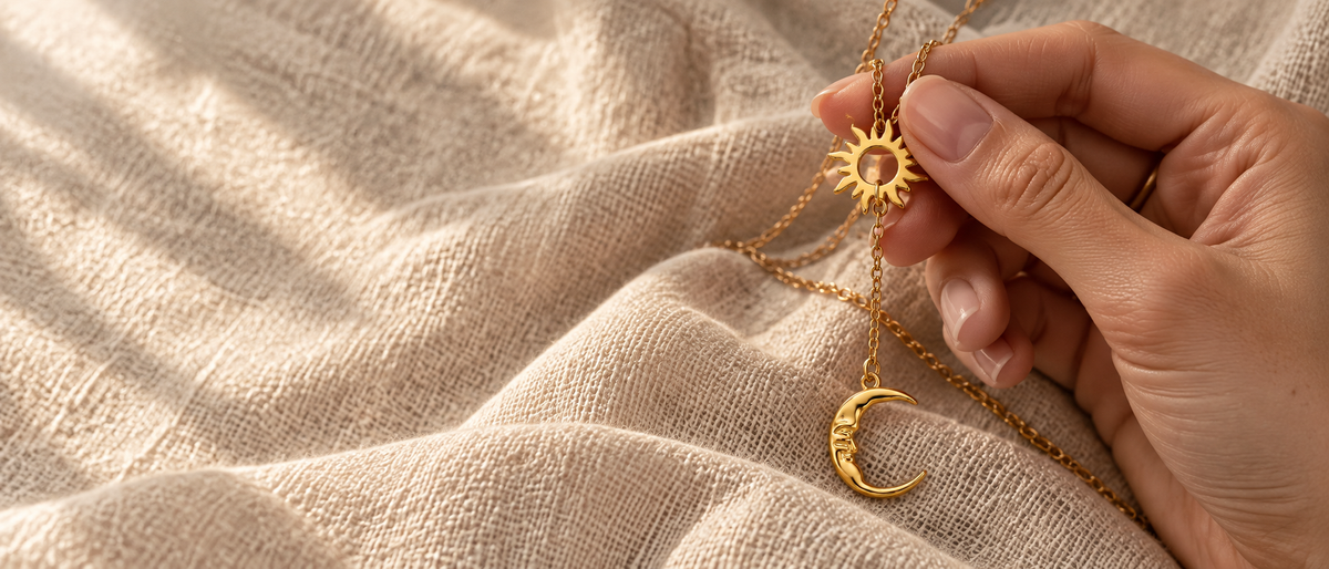 Gold sun and moon Y necklace on oatmeal linen with soft dappled lighting. Celestial pendant with warm golden tones.