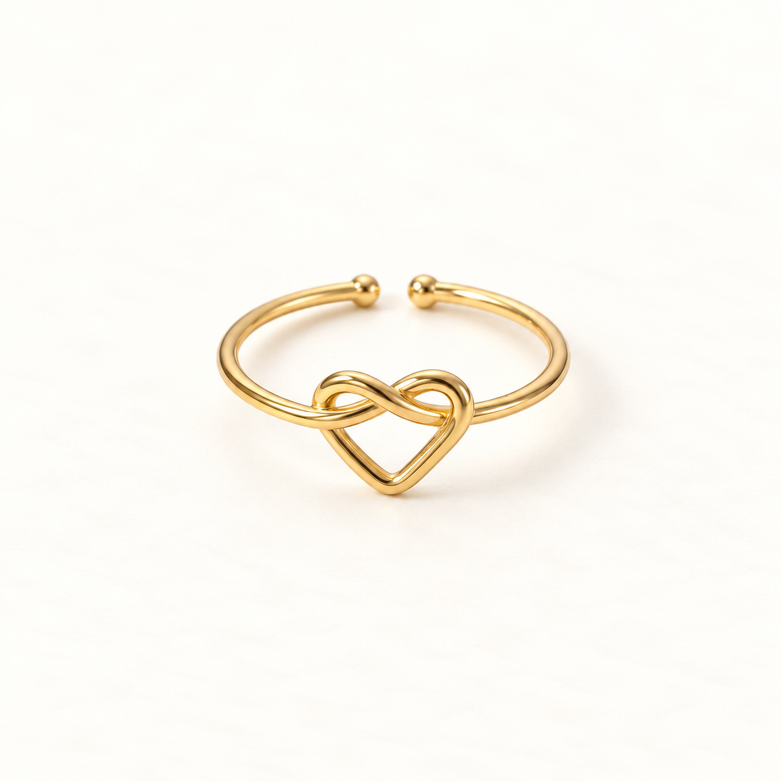 A gold infinity heart ring with continuous loop forming an intertwined heart shape, open adjustable band with textured rope detail, shown from front and side angles on a clean white background displaying the eternal love symbolism, delicate interwoven design, and polished gold finish.