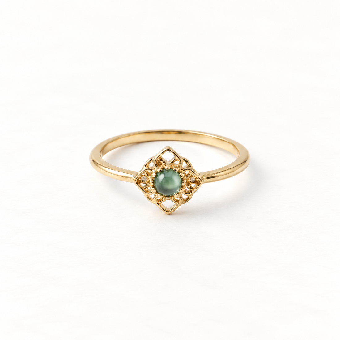 A gold jade filigree ring with green cabochon center stone in diamond-shaped ornate setting, vintage-inspired delicate metalwork with scrolling details, open adjustable band, shown from front and side angles on a clean white background displaying the rich green hue, intricate lace-like frame, and polished gold finish.