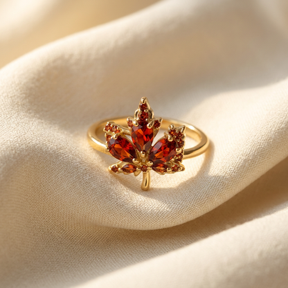A gold maple leaf ring with amber orange citrine stones set in detailed leaf formation lying flat on a white background with soft natural shadows, showing the warm fall hues, intricate stone setting, and polished gold finish from above.