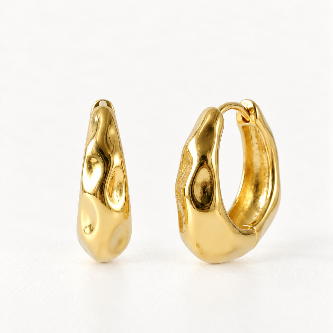 A pair of 18k gold molten lava-textured huggie hoop earrings with organic melted dimpled surface, shown from front and side angles on a clean white background displaying the irregular fluid metal detail and hinged closure.