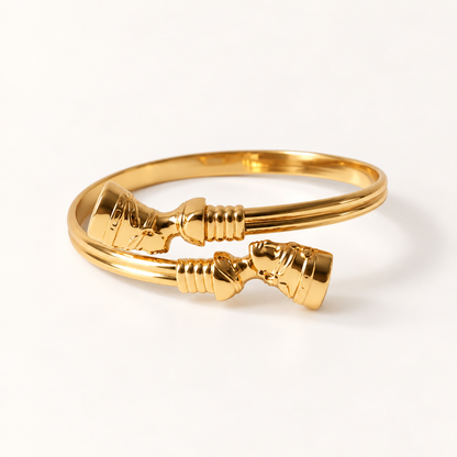 A gold Nefertiti collar bracelet with detailed Egyptian-inspired ribbed texture and ornate cylindrical end caps, shown from front and side angles on a clean white background displaying the open cuff design, regal queen silhouette shape, and intricate end detail.