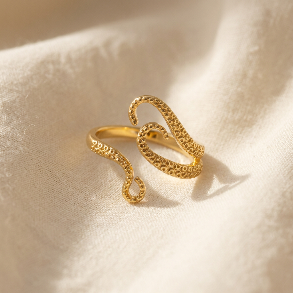 A gold octopus tentacle ring with detailed suction cup texture and curved tentacle arms lying flat on a white background with soft natural shadows, showing the intricate marine texture, organic flowing form, and polished gold finish from above.