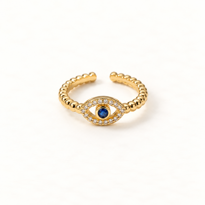 A gold pave evil eye ring with beaded ball chain band, clear crystals surrounding deep blue center stone, and detailed lash design, open adjustable band, shown from front and side angles on a clean white background displaying the protective symbol, sparkling stone detail, and polished gold finish.