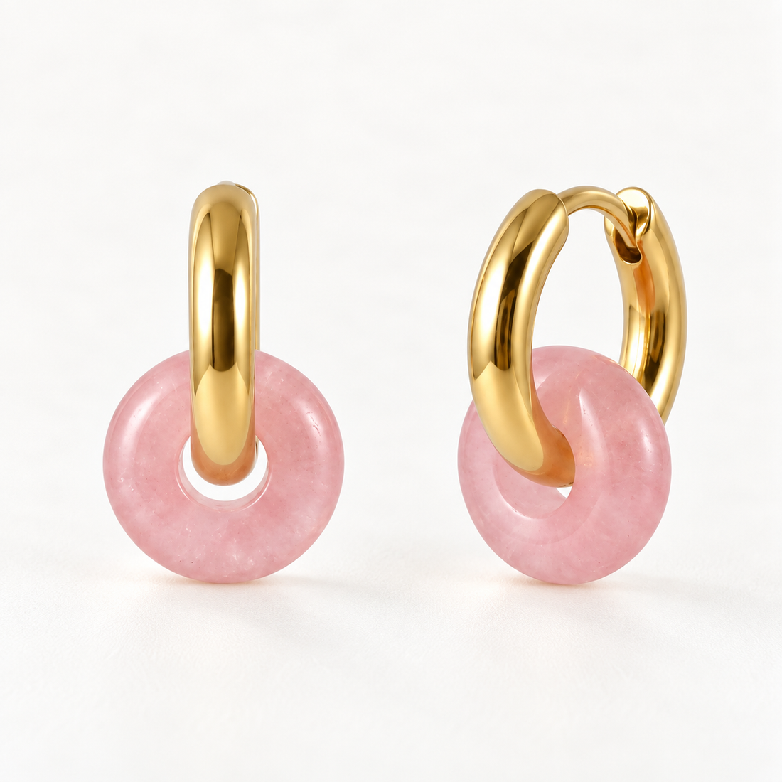A pair of 18k gold huggie hoop earrings with dangling pink jade donut charms, shown from front and side angles on a clean white background displaying the smooth polished pink stone and hinged closure.