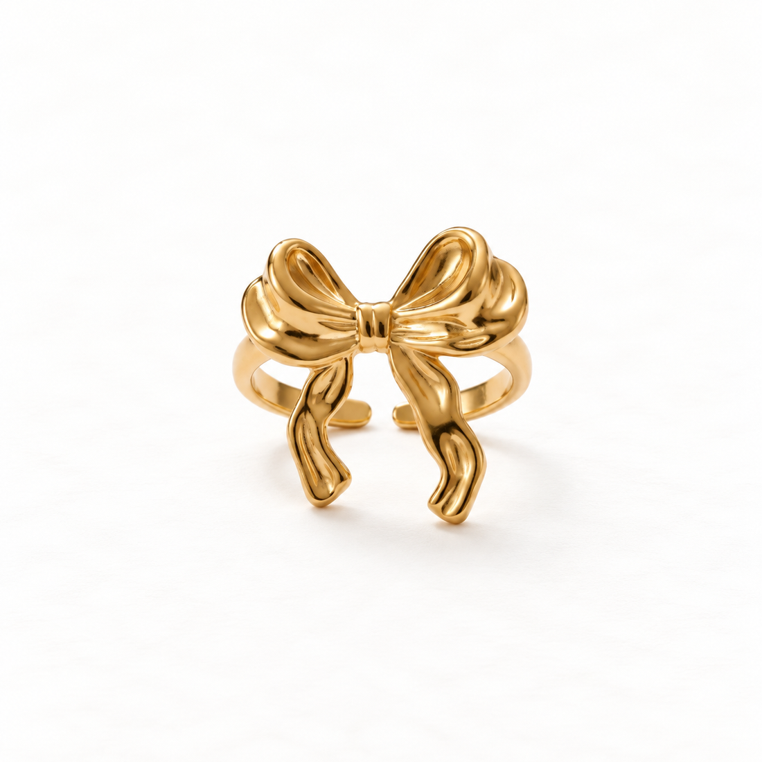 A gold ribbon bow ring with tied bow design featuring two loops and flowing tails, open adjustable band with textured ribbon folds, shown from front and side angles on a clean white background displaying the feminine gift-wrapped aesthetic, detailed fabric texture, and polished gold finish.