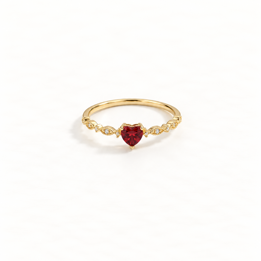 A gold heart ring with deep red ruby center stone and clear crystal accents on delicate band, romantic design with faceted gemstone, open adjustable band, shown from front and side angles on a clean white background displaying the passionate red hue, sparkling stone setting, and polished gold finish.