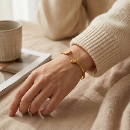 Close-up of a feminine wrist wearing a gold snake cuff bracelet with textured scale pattern, the serpent head resting on the wrist bone with the curved tail wrapping around. Soft natural lighting, warm beige linen background, natural skin texture with visible pores and slight imperfections.